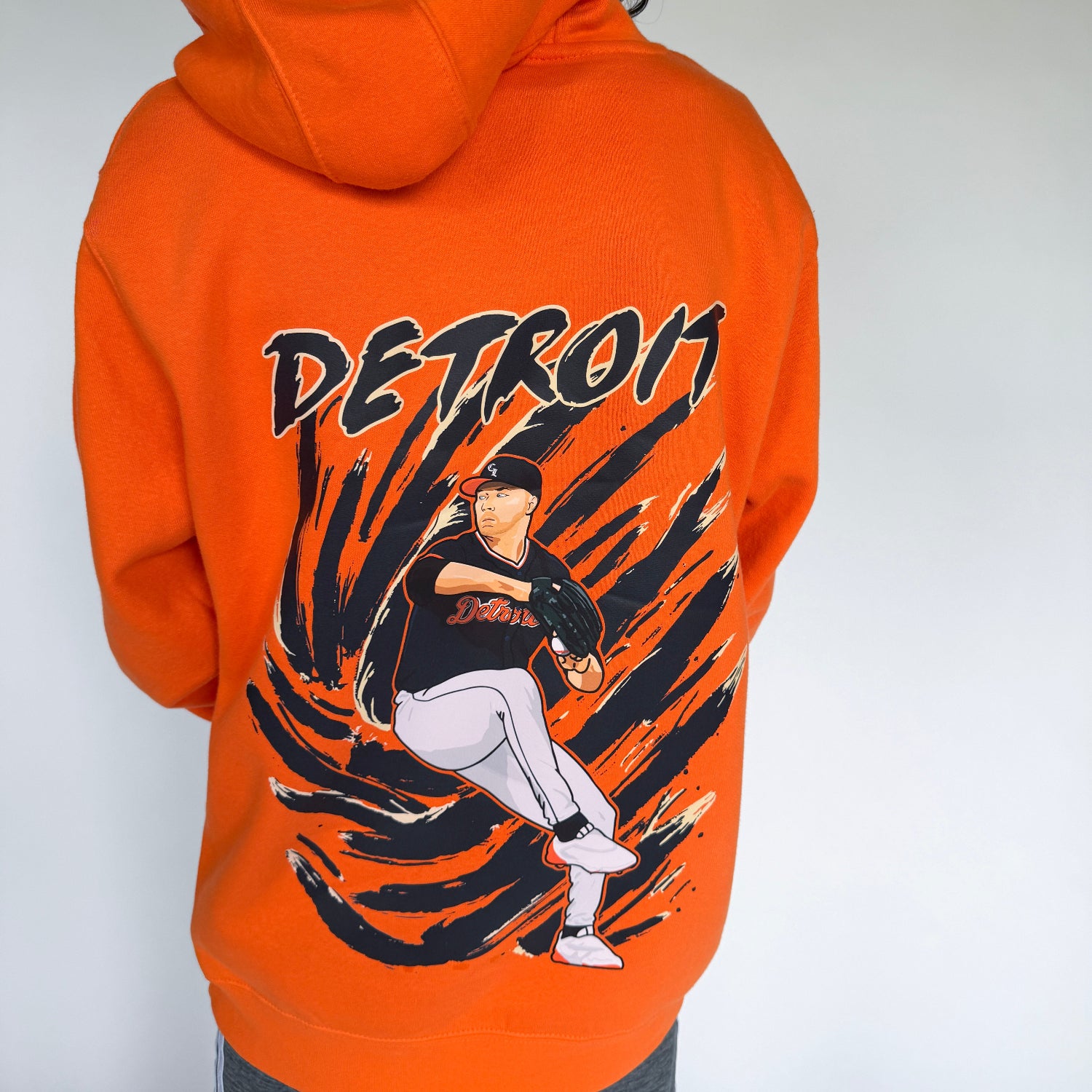 Person wearing an orange hoodie with 'Detroit' and a baseball player graphic on the back.